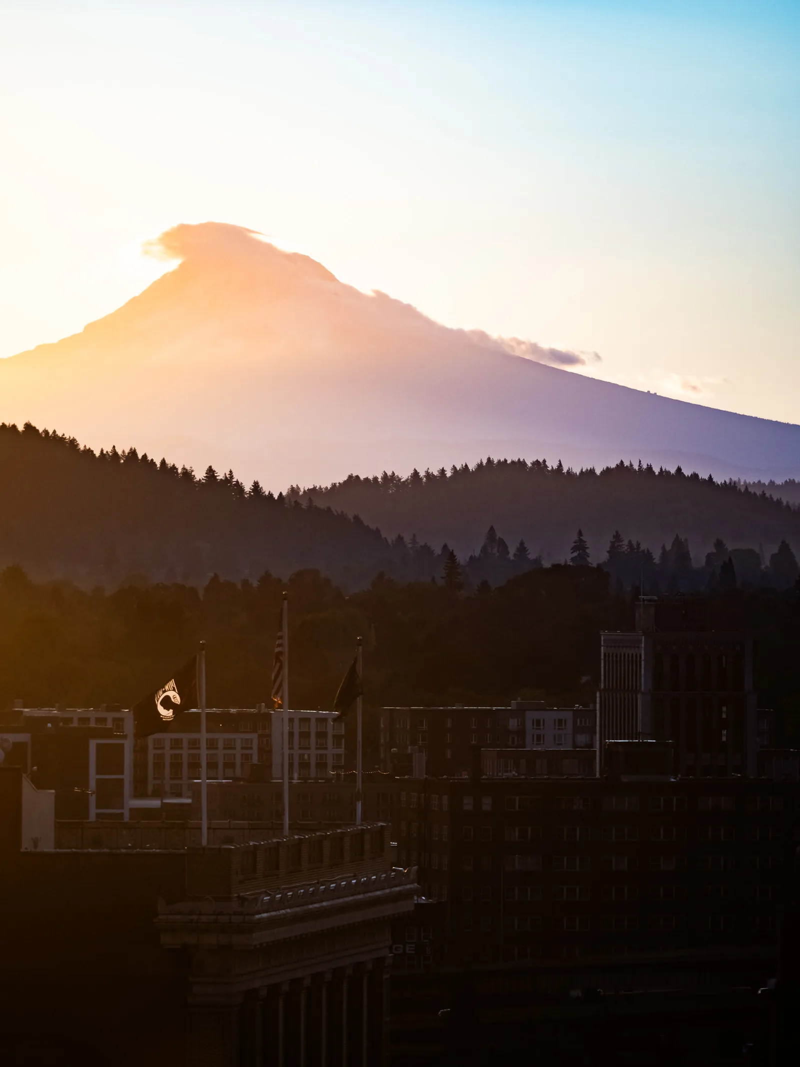 Mt. Hood glowing pink at sunrise above dark hills and rooftops.