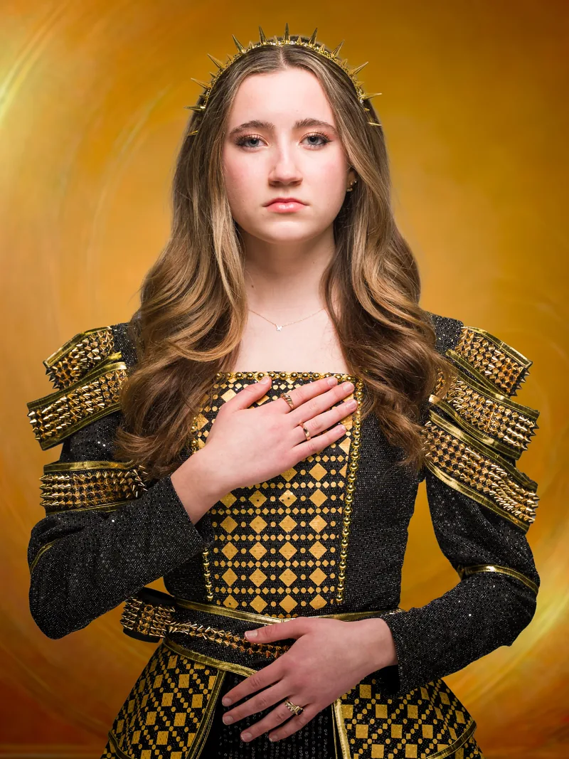 Character portrait of Catherine of Aragon from SIX, in a gold-studded costume and crown against a glowing gold background.