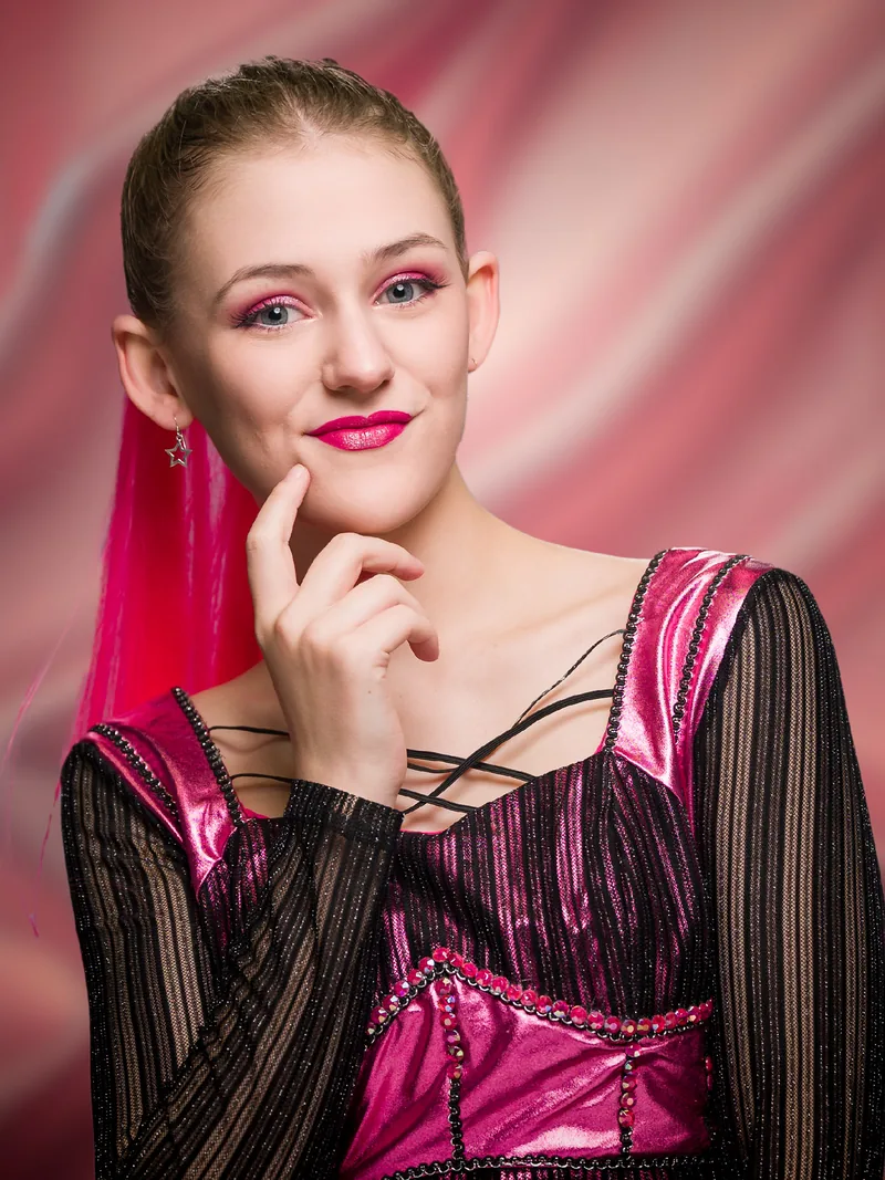 Character portrait of Katherine Howard from SIX, finger to chin in a pink costume against a pink background.