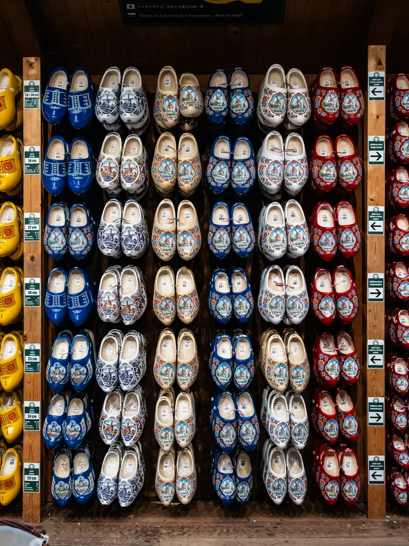 Rows of painted wooden clogs, blue, white and red, displayed on a wall.