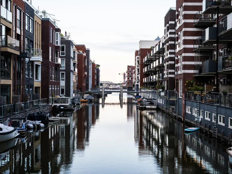 A straight canal between modern brick apartment buildings, their balconies reflected in still water.