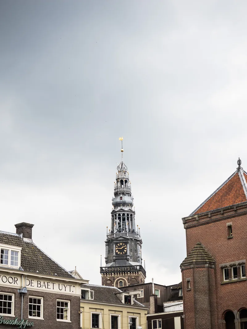 A church clock tower between brick buildings under a grey sky.