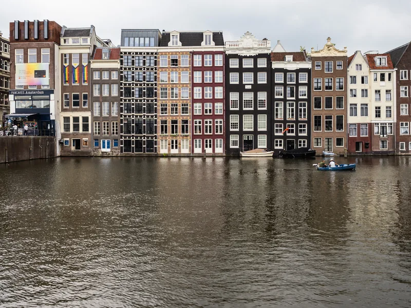 A row of narrow canal houses in brick and white facing the water on an overcast day.