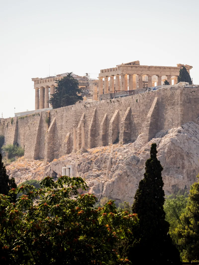The Acropolis and its ancient temples above sheer rock walls, with cypress trees below.