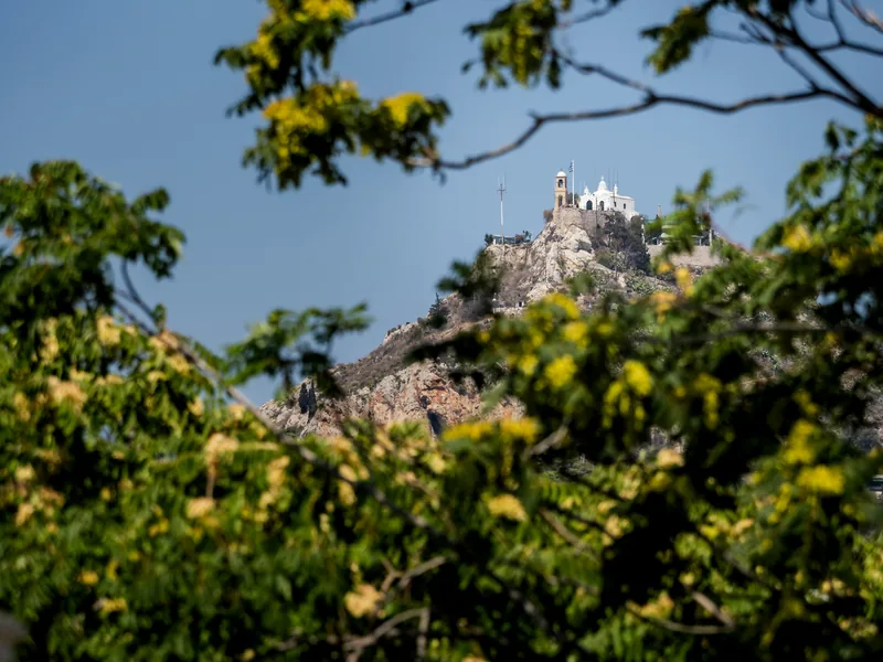 A small white chapel on top of Mount Lycabettus, framed by green leaves.