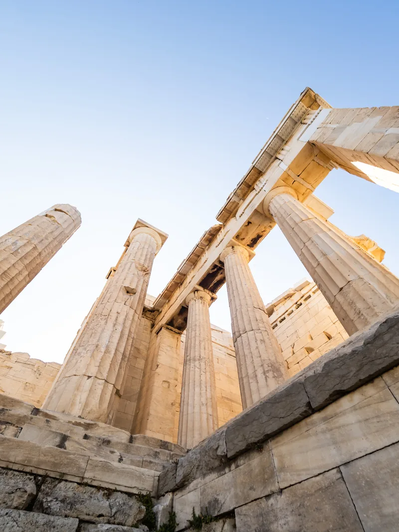 Marble columns of the Propylaea rising against a blue sky, seen from below.