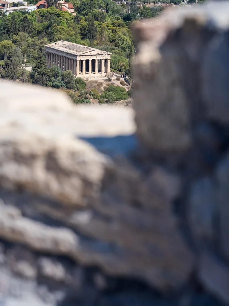 The Temple of Hephaestus on a wooded hill, seen past blurred stone in the foreground.