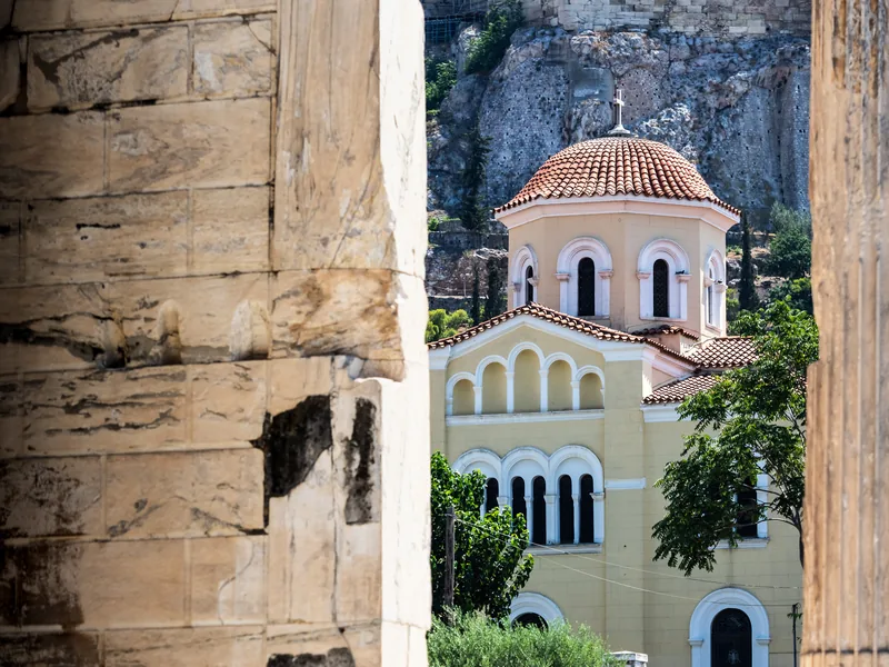 A yellow Orthodox church with a red-tiled dome framed between weathered marble columns.