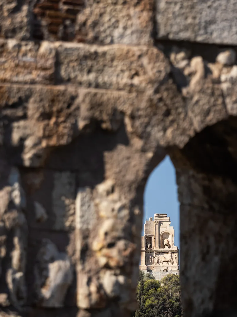 A glimpse of a hilltop monument through a worn stone arch.