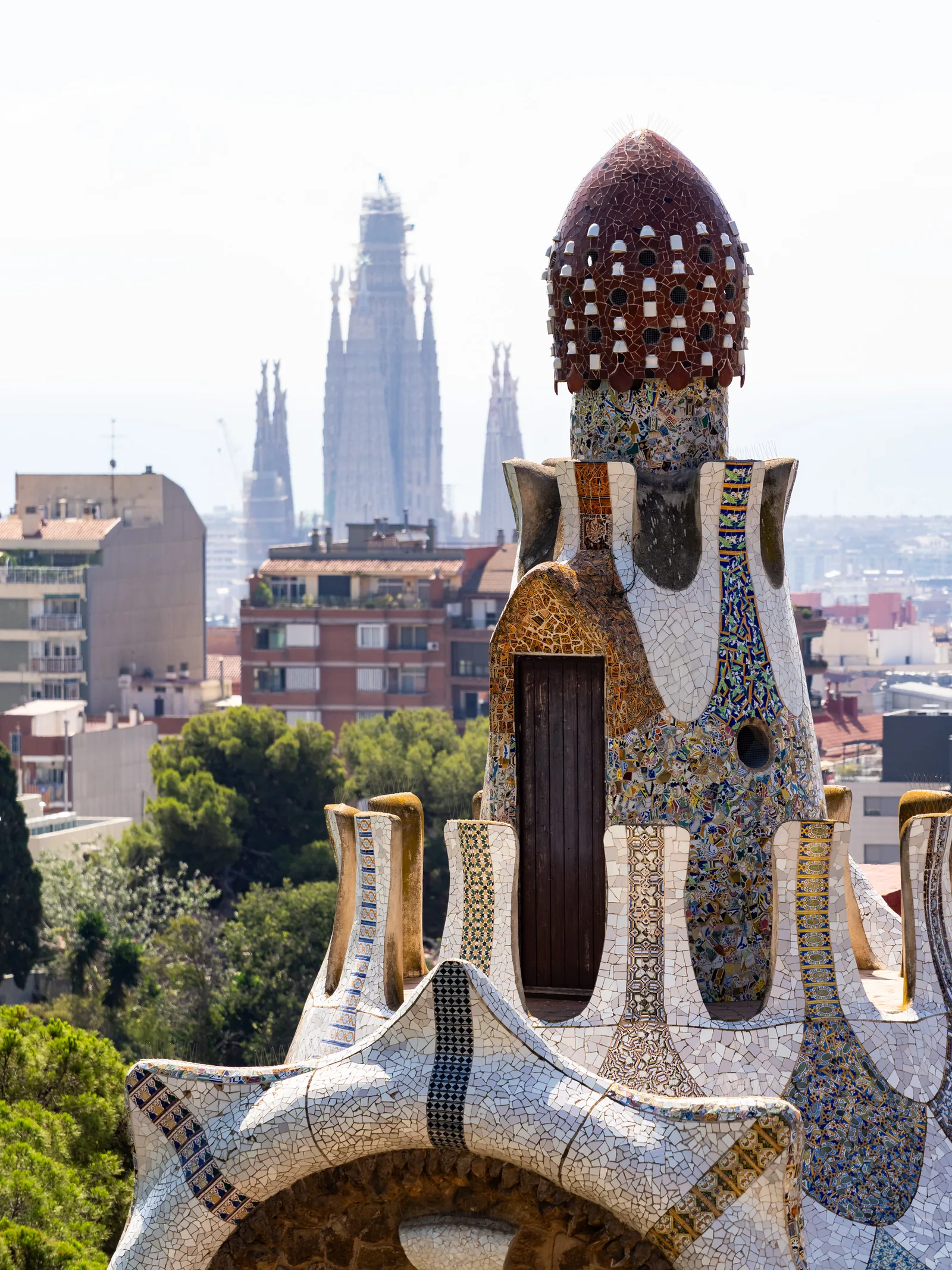 A mosaic-covered Gaudí tower at Park Güell, with Sagrada Família's spires rising in the distance.
