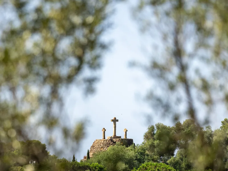 Three stone crosses on a rocky hilltop, framed by softly blurred branches.