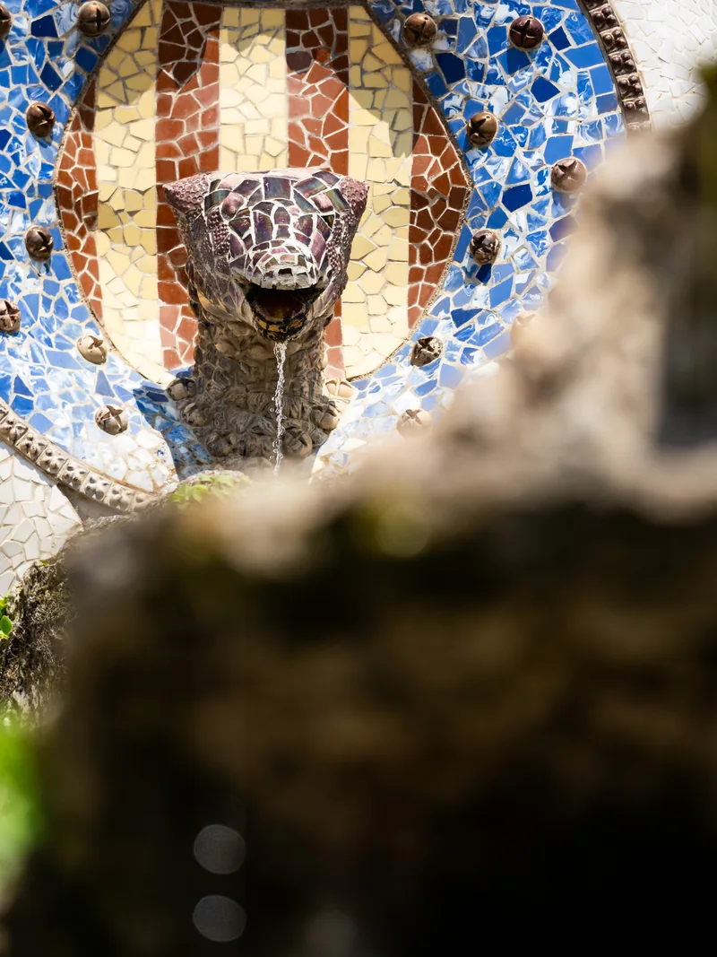 Gaudí's mosaic serpent fountain against a striped red and gold tiled crest.