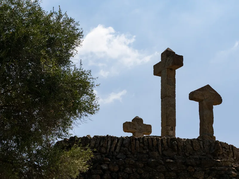 Stone crosses silhouetted on a rough stone mound against a blue sky with a tree to one side.
