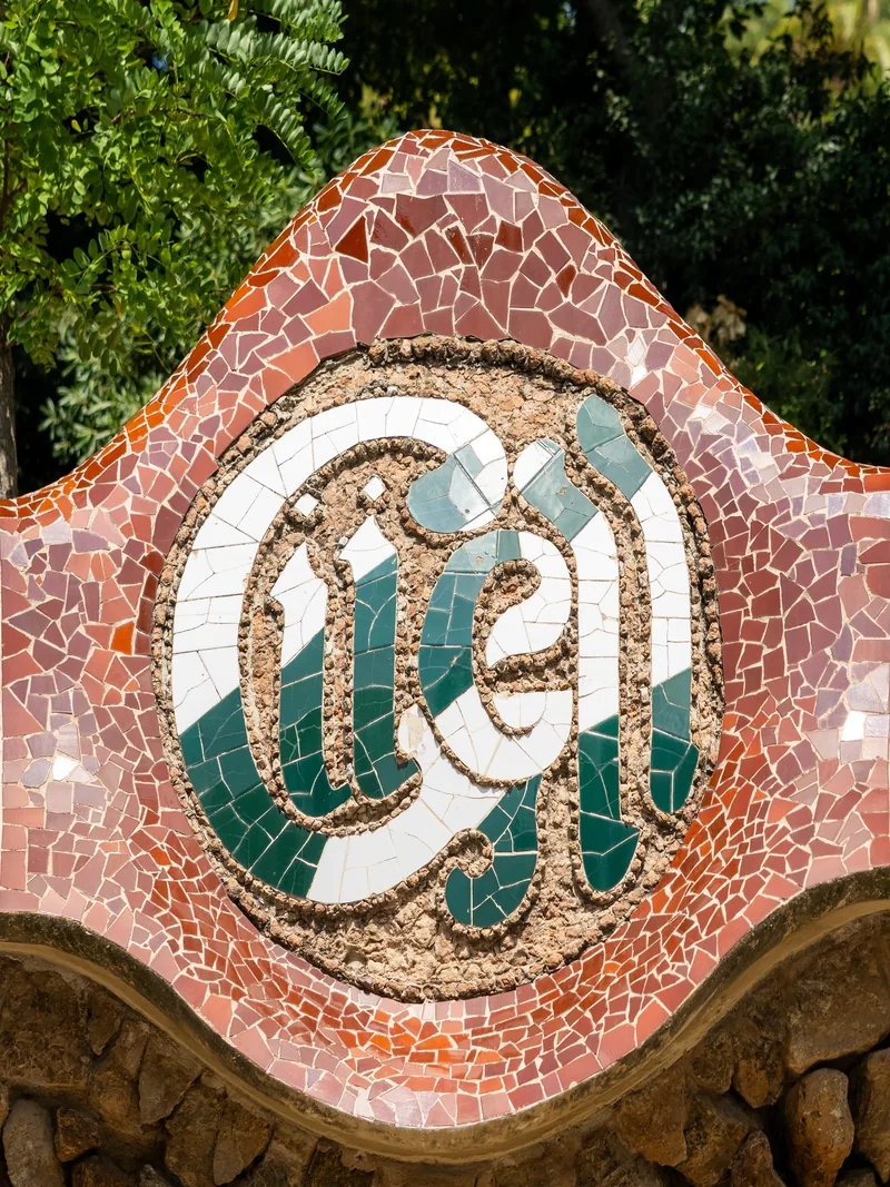 A curved mosaic medallion in red, white and green tile set in a park wall.