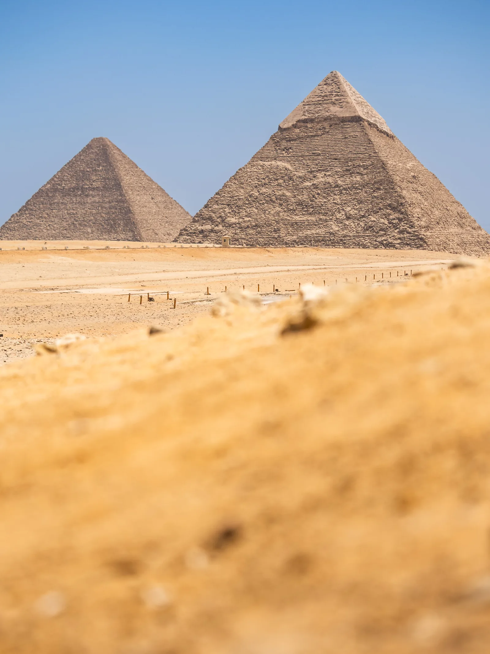 Two of the Giza pyramids rising beyond soft-focus desert sand.