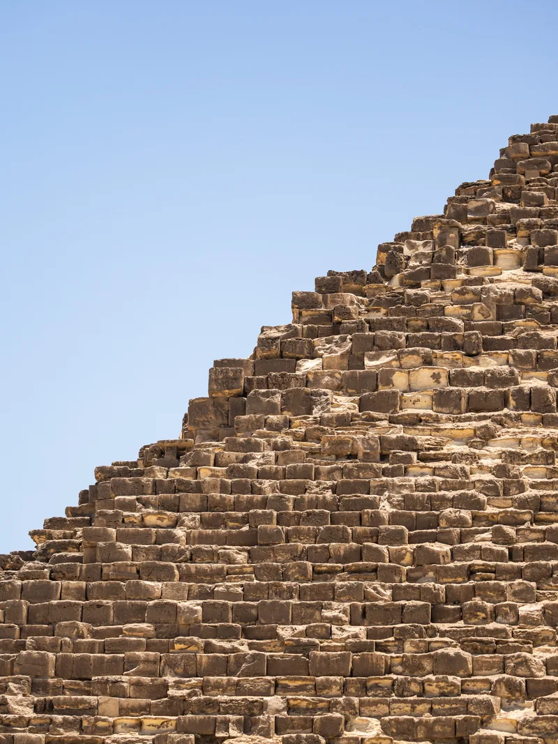 The stepped limestone blocks of a pyramid's edge against a pale blue sky.