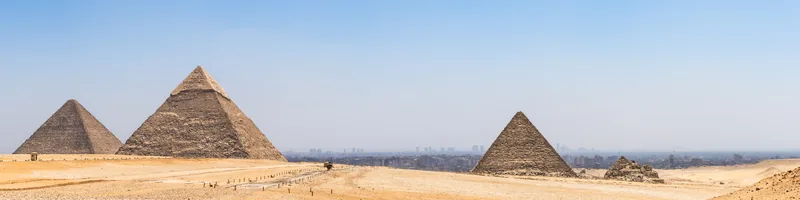 A panorama of the Giza pyramids across the desert, with Cairo's skyline hazy on the horizon.