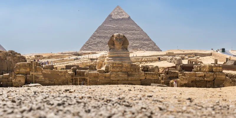 The Great Sphinx in front of the Pyramid of Khafre, seen from low across gravel.