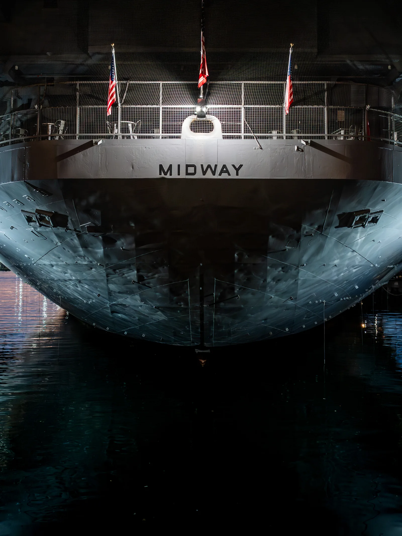 The stern of the USS Midway lit up at night above dark water.