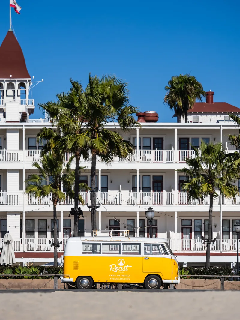 A yellow VW bus parked in front of the white Hotel del Coronado and its palm trees.