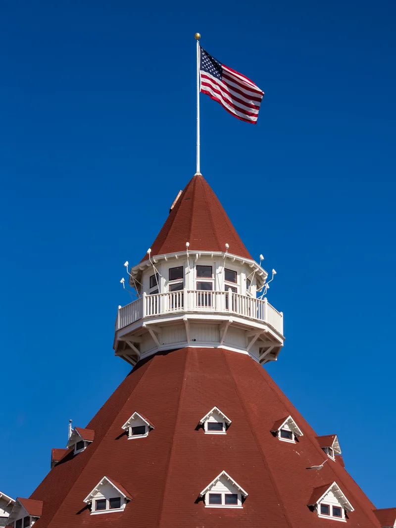 An American flag above Hotel del Coronado's red turret against a deep blue sky.