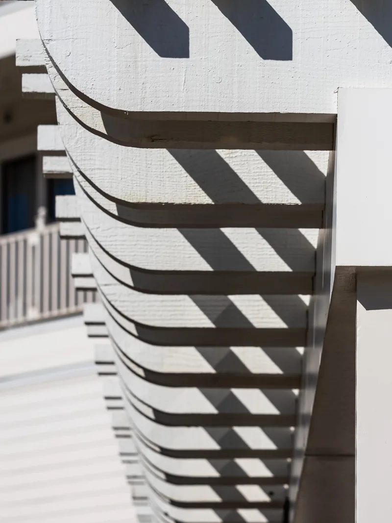 Bold diagonal shadows across curved white wooden trim.