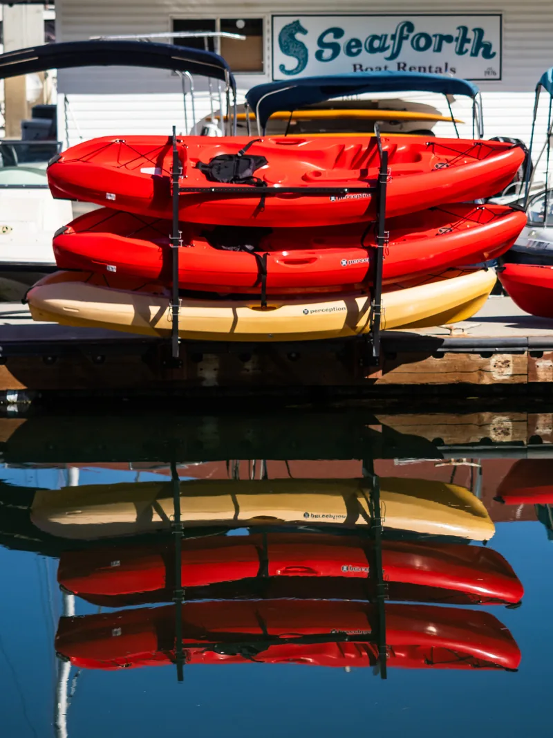 Stacked red and yellow kayaks reflected in the water at a rental dock.