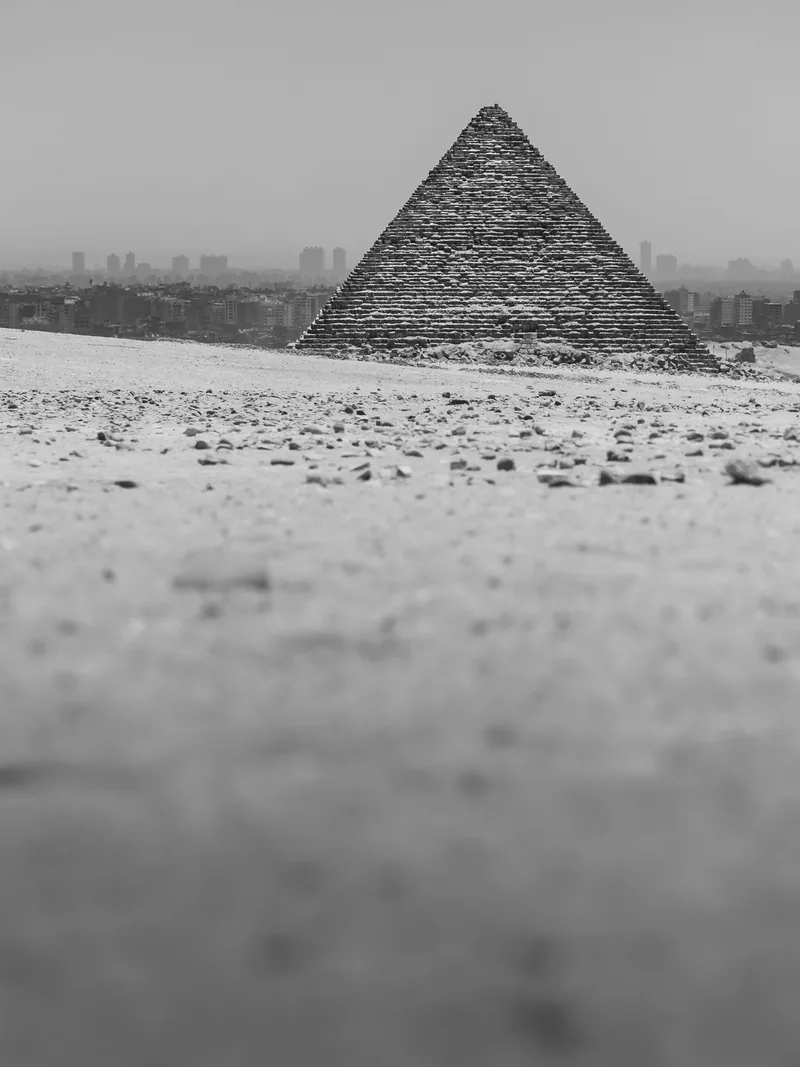 A small Giza pyramid on the horizon beyond the sand, in black and white.