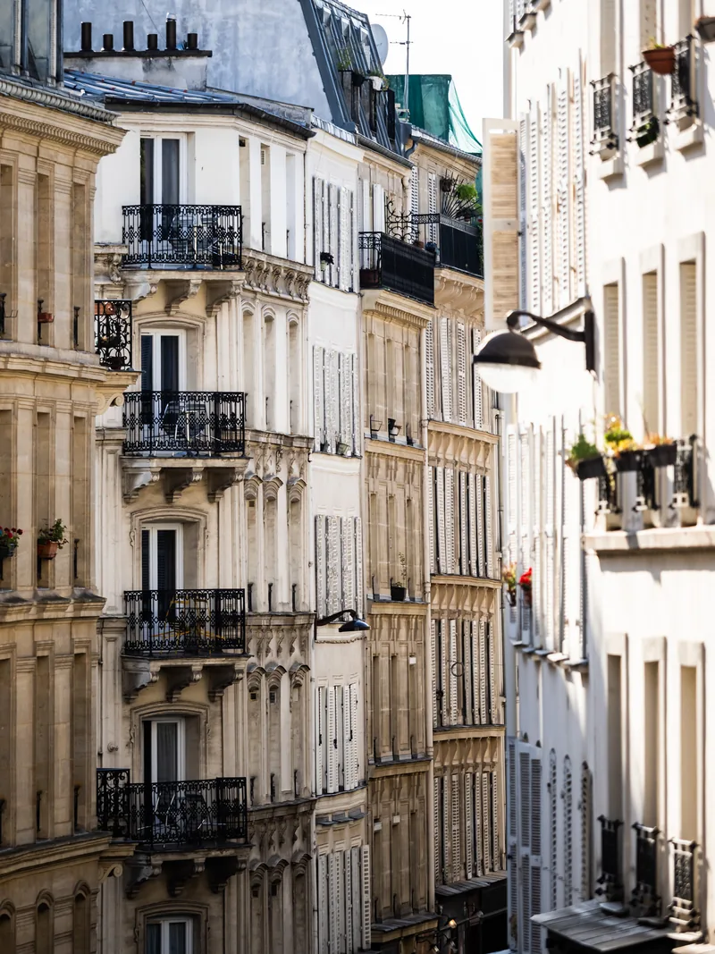 Tall cream apartment buildings with wrought-iron balconies along a Paris street.