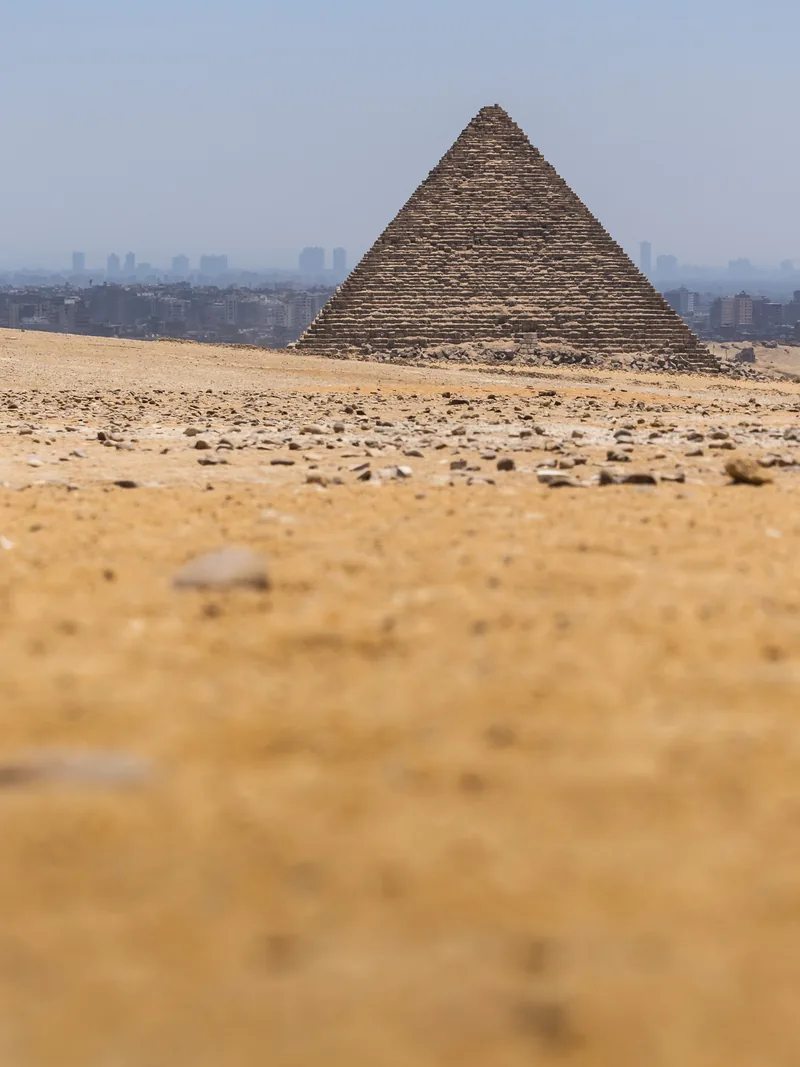 A small pyramid on the desert horizon at Giza, seen from ground level across the sand.
