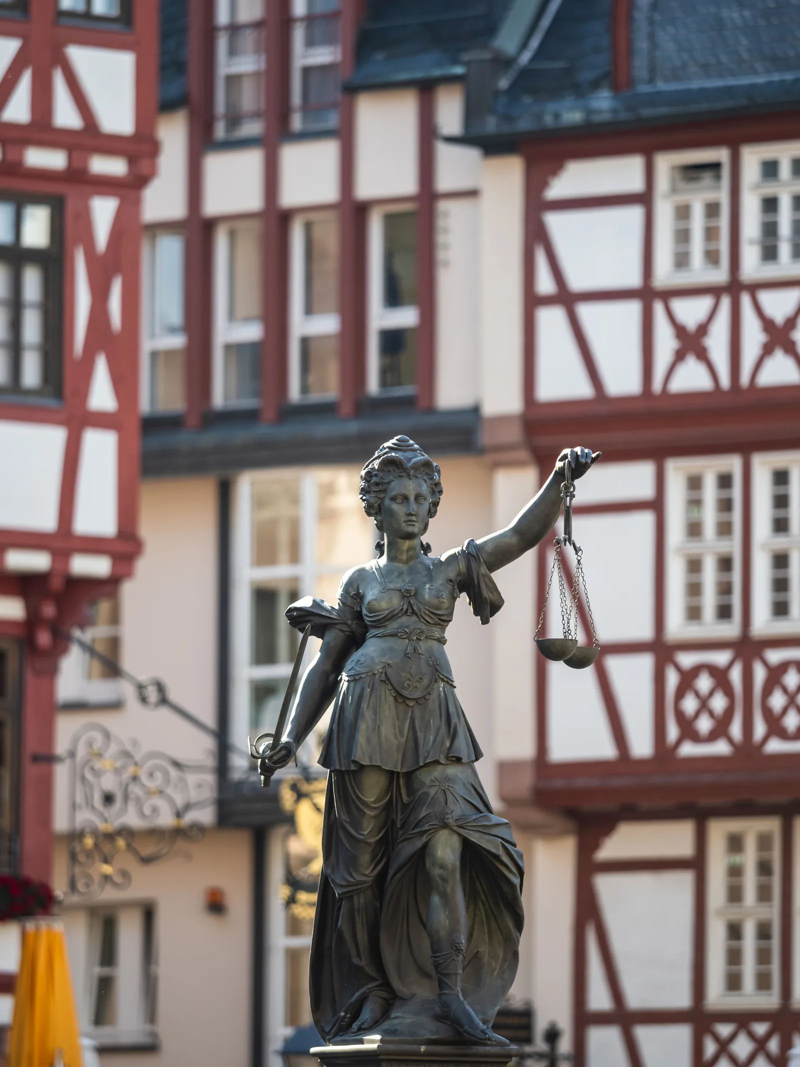 The bronze Justitia statue with her scales in front of red half-timbered houses on the Römerberg.