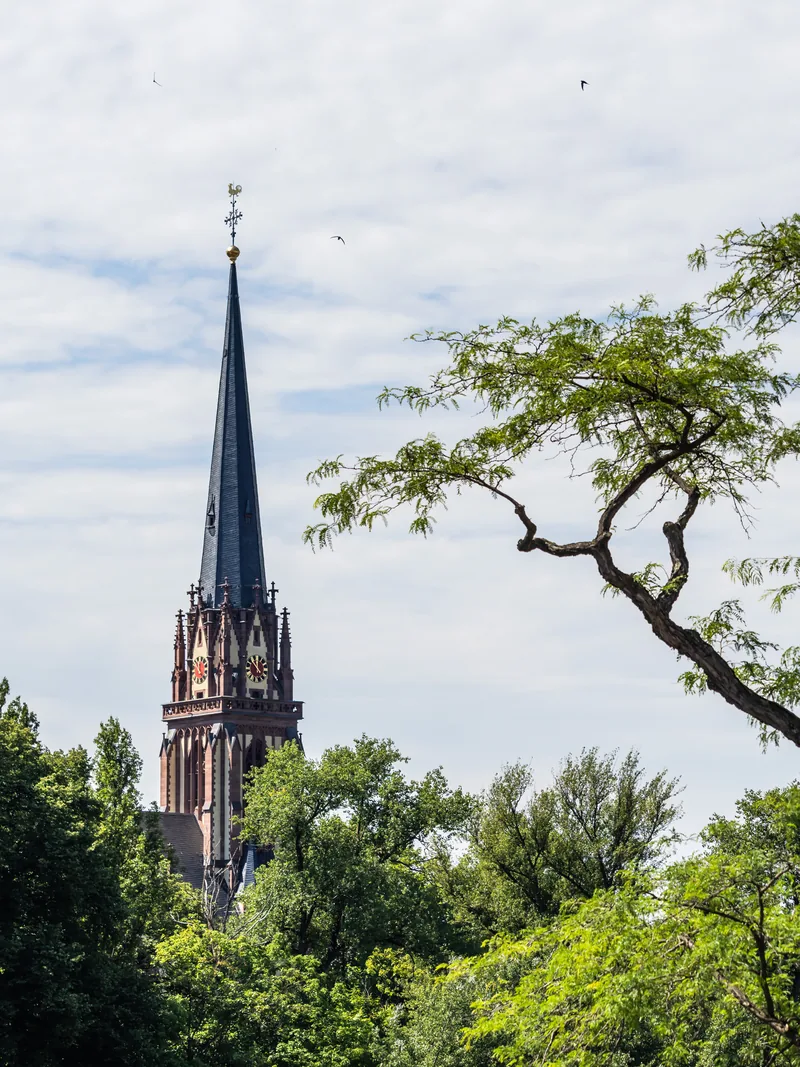 A tall dark church spire rising above green treetops.