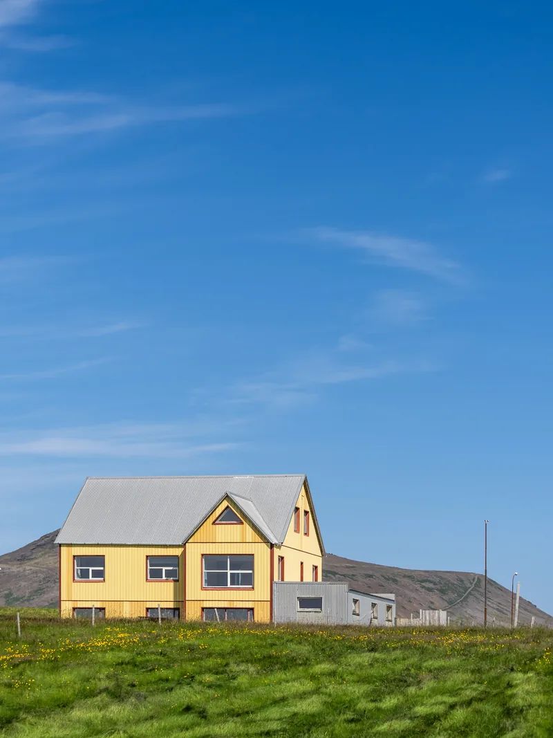 A yellow house with a grey roof alone on a green field under a deep blue sky.