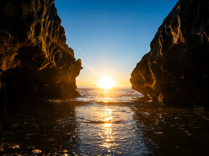 The setting sun framed between two rock formations over the water.