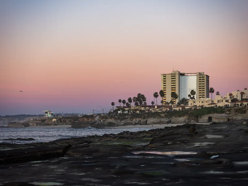 A pink sky over the La Jolla coastline and a hotel tower at dusk.