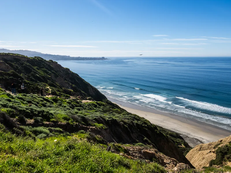 Green bluffs dropping to a wide beach with the ocean beyond.
