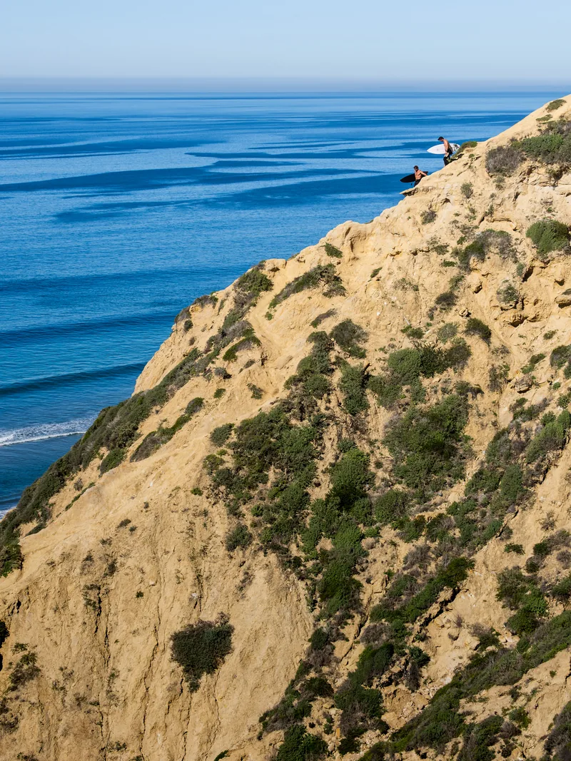 A sandy cliff face covered in scrub above the blue Pacific.