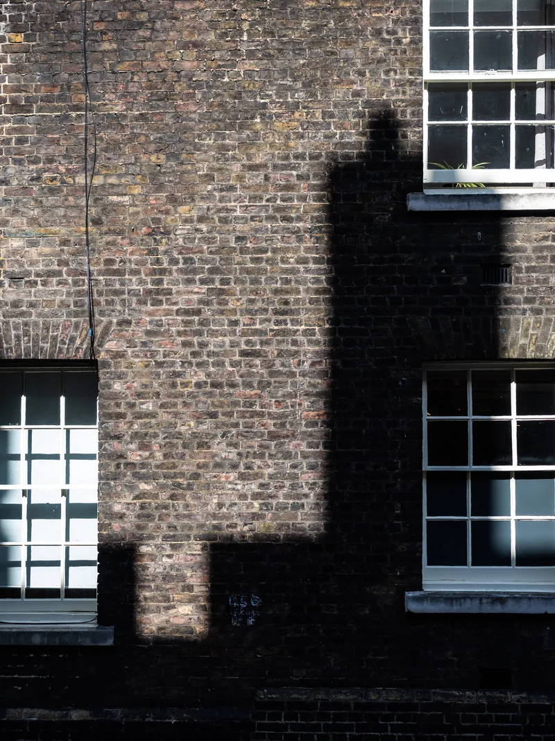 A stepped shadow falling across a brick wall between white-framed Georgian windows.