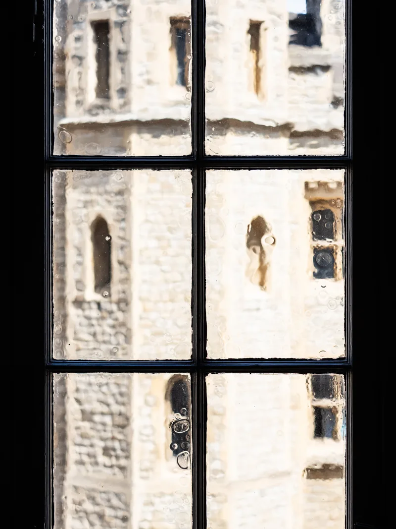 Pale medieval stonework seen through the panes of a dark, old window frame.