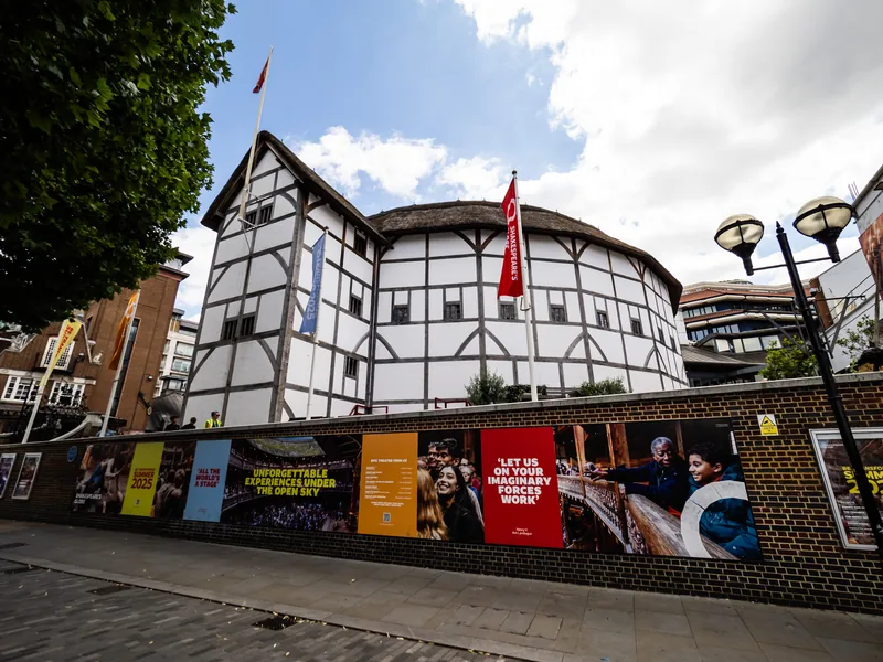 The white timber-framed walls of Shakespeare's Globe above a street lined with colourful theatre posters.