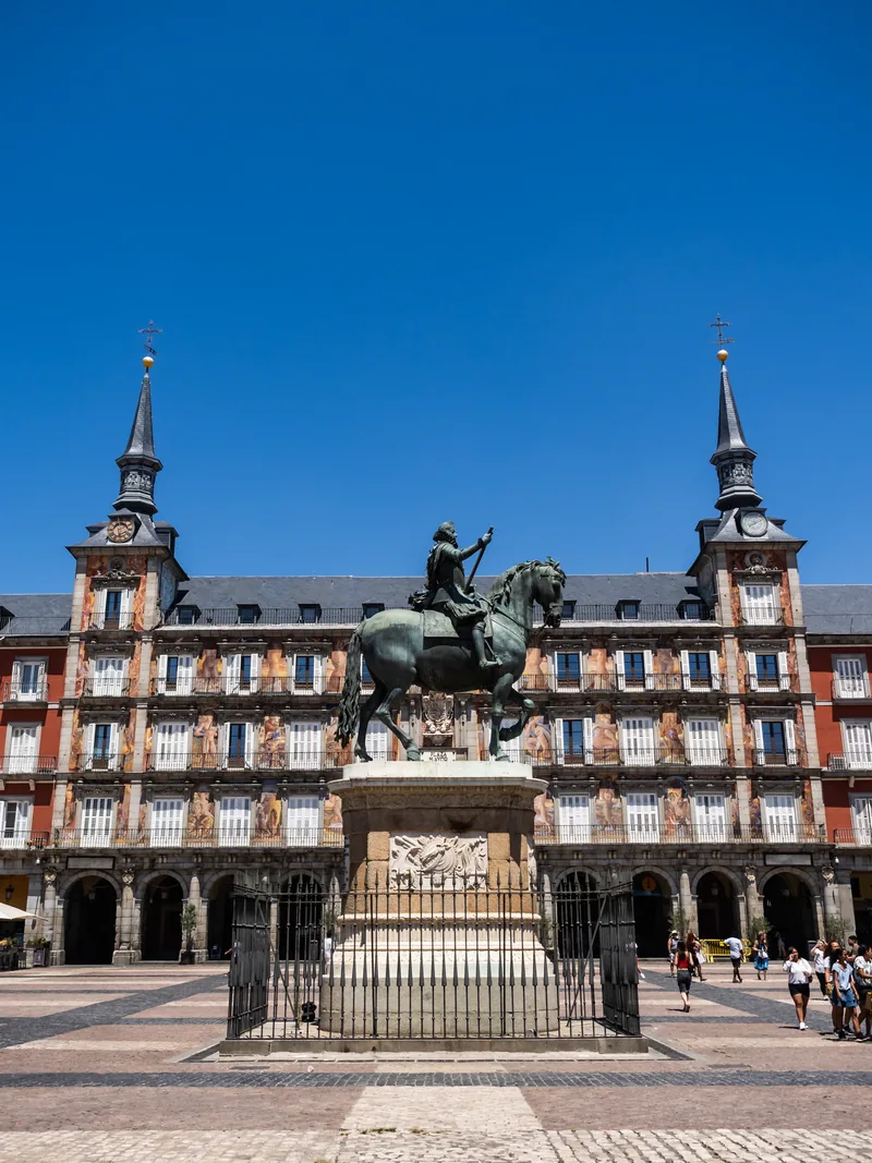 Plaza Mayor's statue of Philip III in front of the painted Casa de la Panadería under a deep blue sky.
