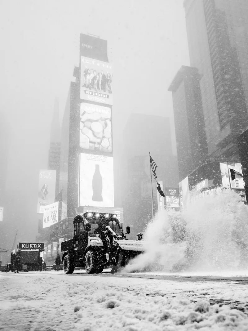 A snowplow pushing snow through Times Square in a blizzard, in black and white.