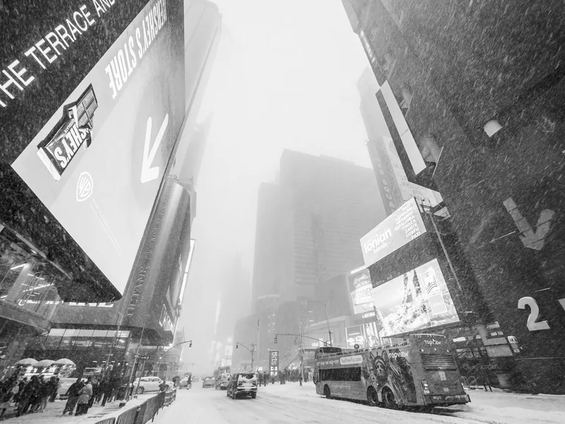 Times Square billboards and a tour bus fading into falling snow.