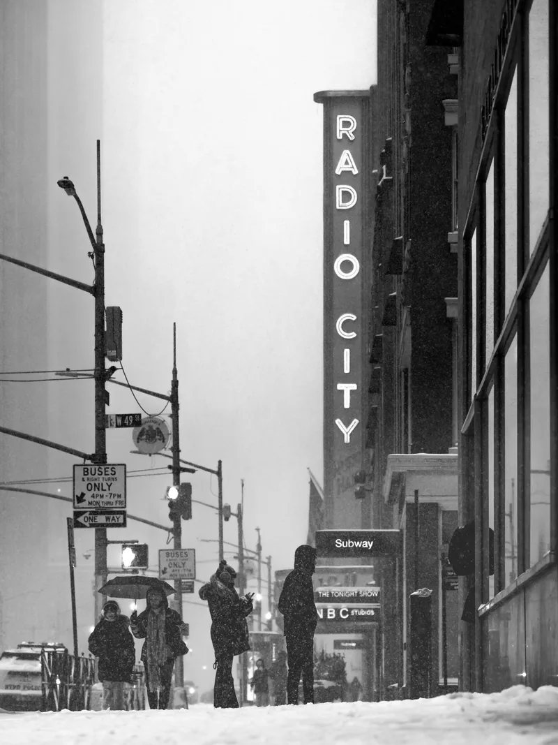 The Radio City sign above people waiting at a snowy corner.