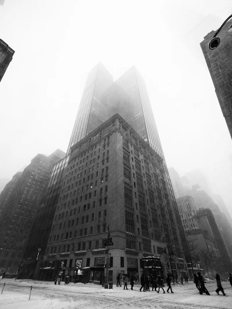 An office tower disappearing into snow and fog, with pedestrians below.