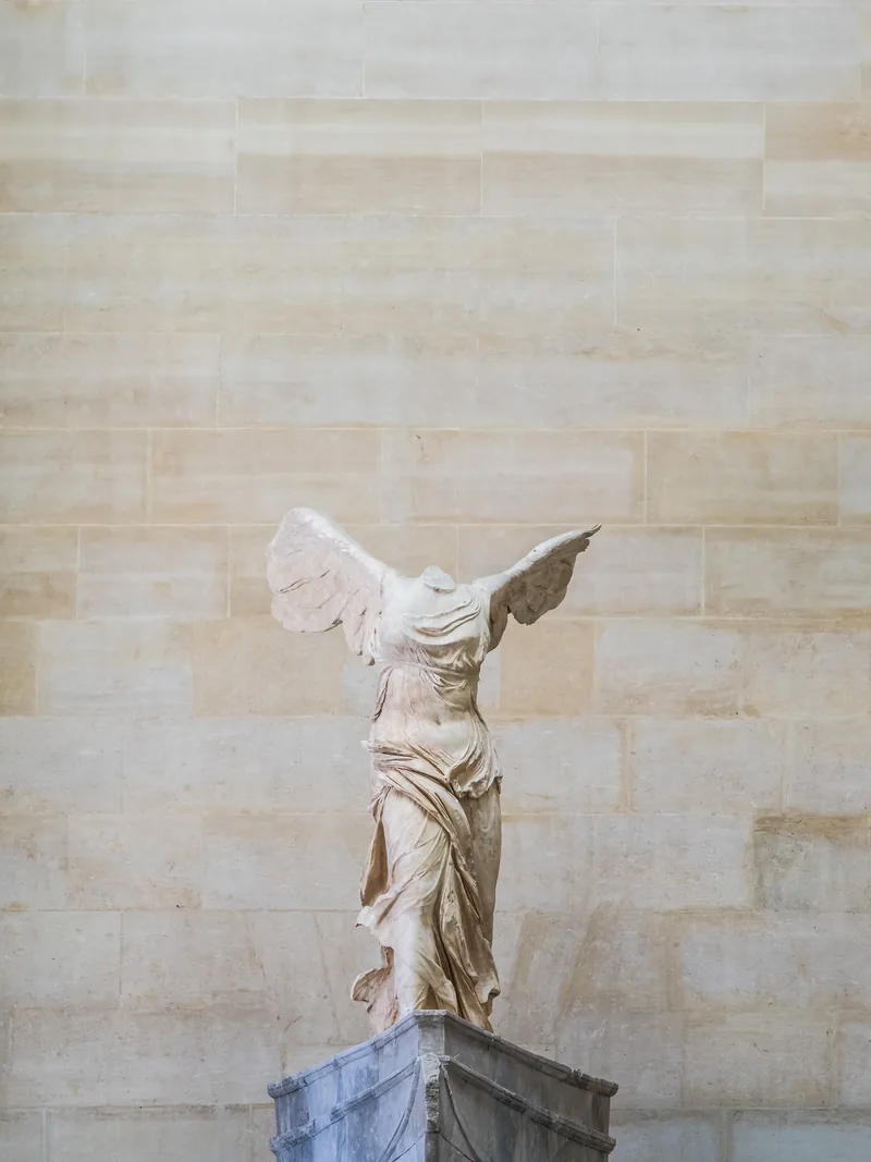 The Winged Victory of Samothrace on its stone base in soft light.