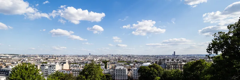 A wide view over the rooftops of Paris under scattered white clouds.
