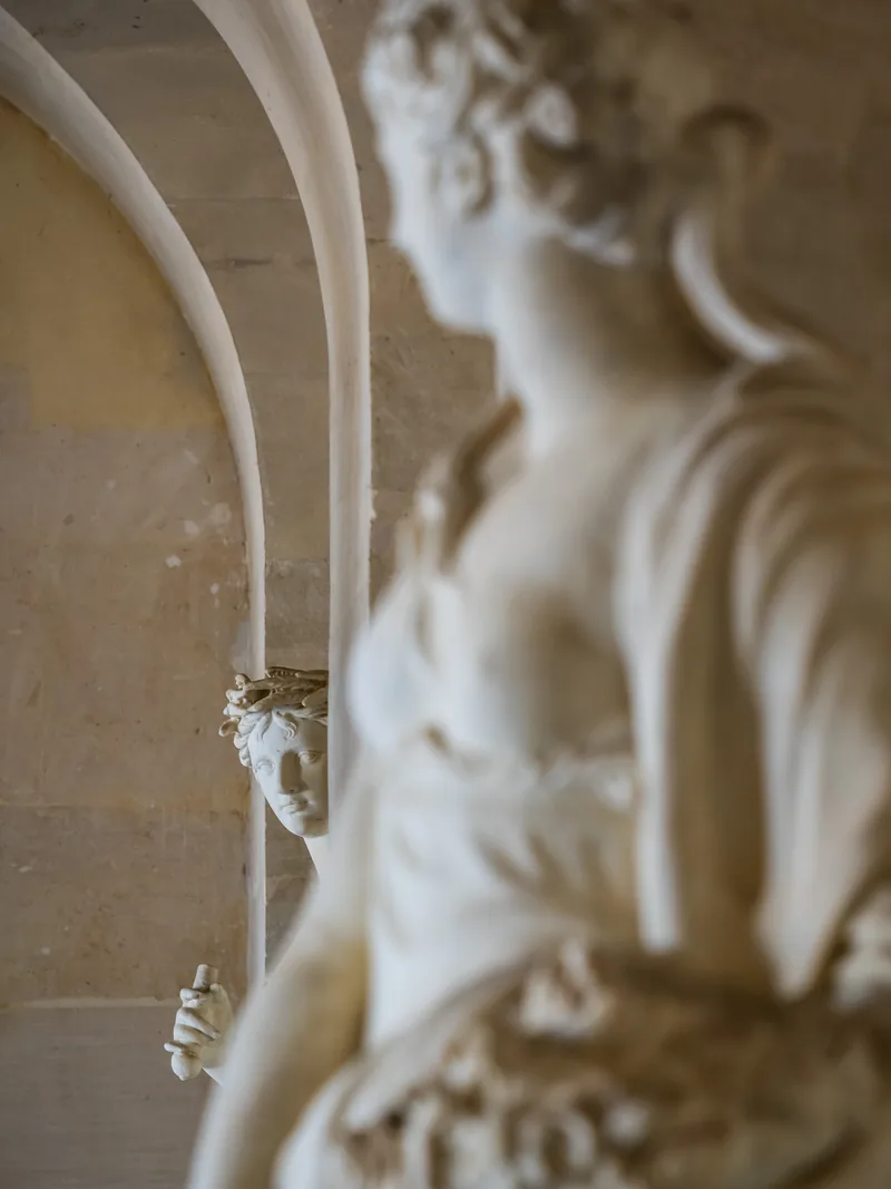 A marble statue in soft focus in the foreground of an arched stone gallery.