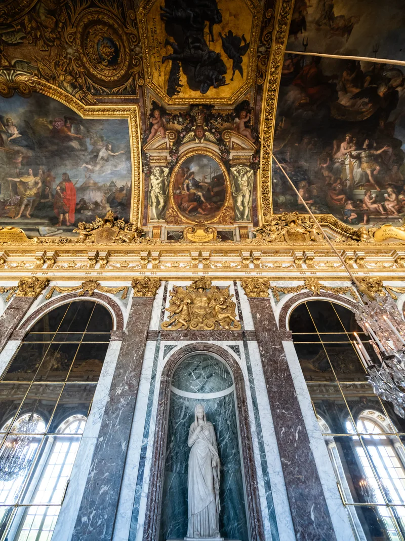 The painted, gilded ceiling and mirrored arches of the Hall of Mirrors at Versailles.