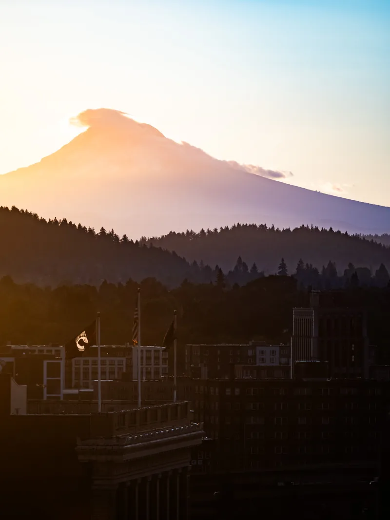 Mt. Hood glowing pink at sunrise above dark hills and rooftops.